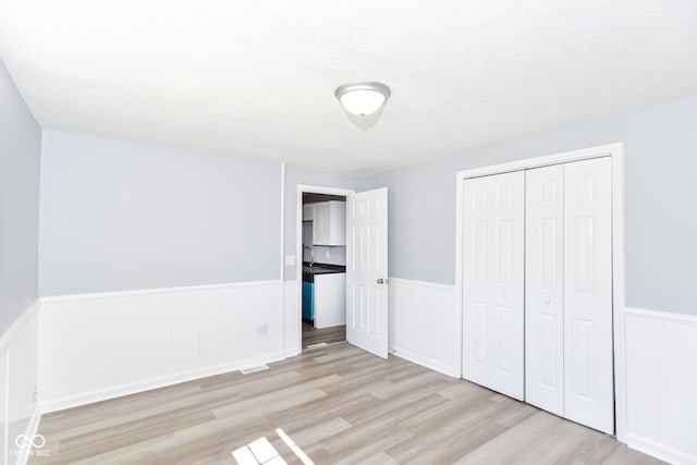 unfurnished bedroom with a wainscoted wall, light wood finished floors, and a closet