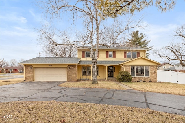 traditional home featuring brick siding, an attached garage, fence, and aphalt driveway