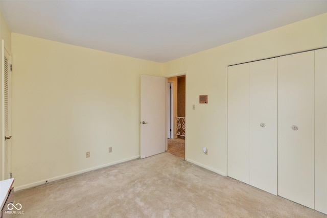 unfurnished bedroom with a closet, light colored carpet, and baseboards