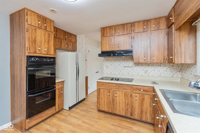 kitchen with under cabinet range hood, light countertops, light wood-type flooring, black appliances, and a sink