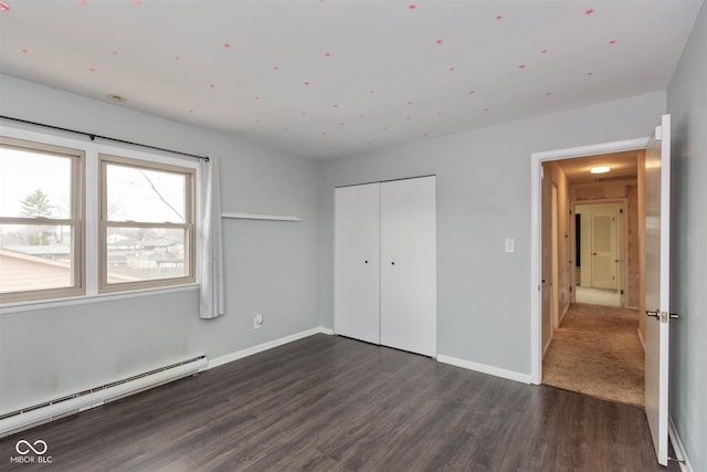 unfurnished bedroom featuring dark wood-style floors, baseboards, baseboard heating, and a closet