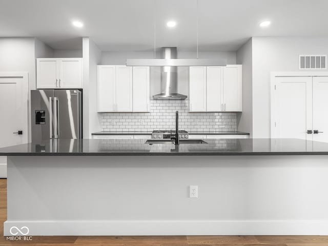 kitchen featuring stainless steel fridge, visible vents, white cabinets, a spacious island, and wall chimney range hood