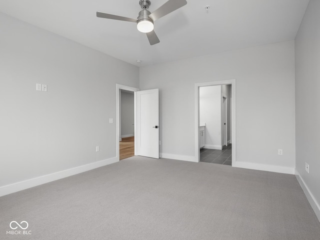 unfurnished bedroom with ensuite bath, baseboards, and dark carpet