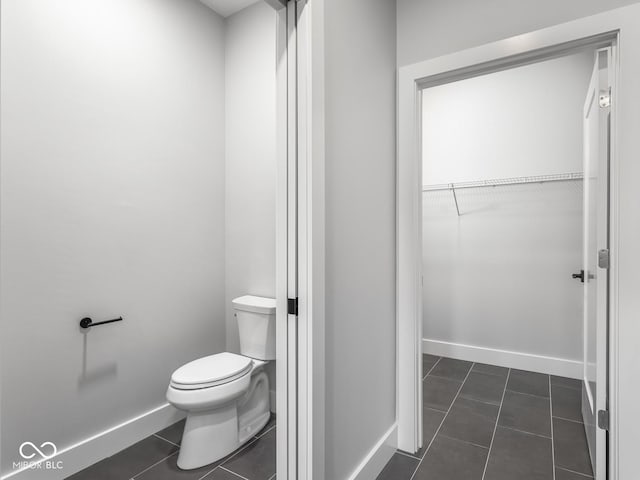 bathroom featuring baseboards, a walk in closet, toilet, and tile patterned floors