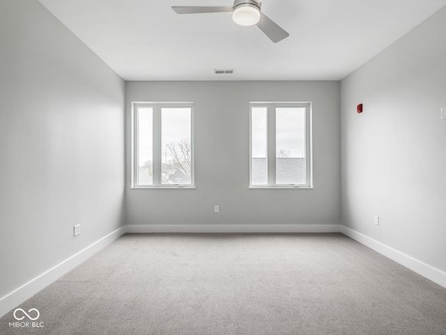 carpeted spare room with visible vents, baseboards, and a ceiling fan