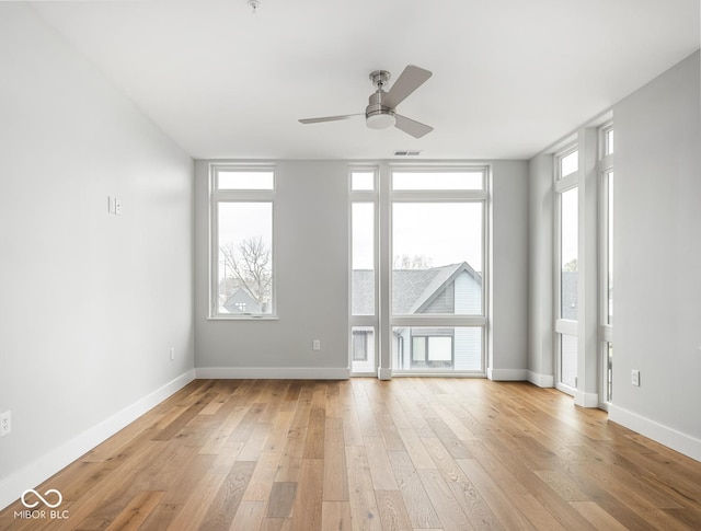 spare room with light wood finished floors, a ceiling fan, visible vents, and baseboards