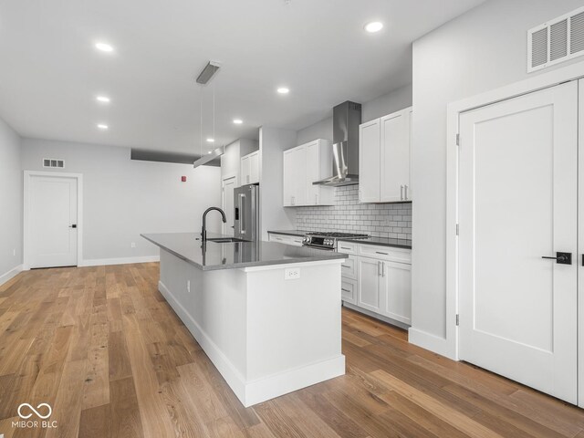 kitchen with wall chimney range hood, visible vents, light wood-style floors, and a sink