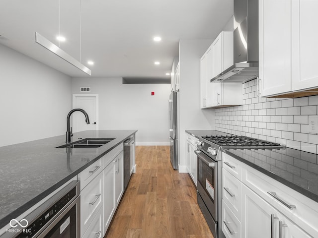 kitchen with wall chimney exhaust hood, appliances with stainless steel finishes, a sink, and white cabinetry