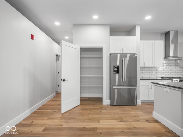 kitchen with tasteful backsplash, white cabinets, light wood-style flooring, wall chimney range hood, and stainless steel refrigerator with ice dispenser