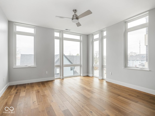 unfurnished room with light wood-style flooring, a wall of windows, visible vents, and baseboards