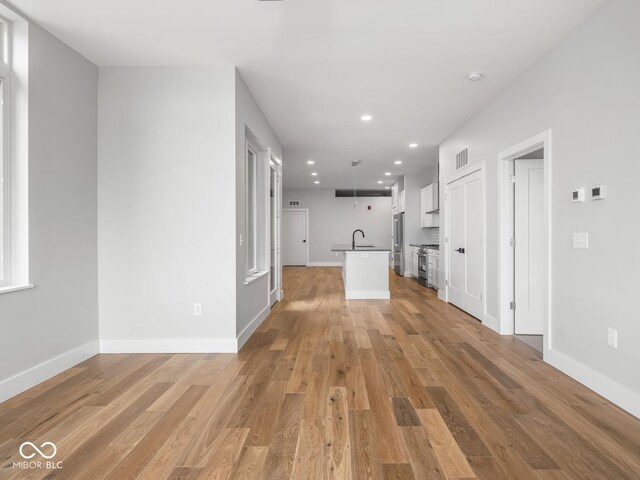 unfurnished living room featuring light wood-style floors, visible vents, a sink, and baseboards