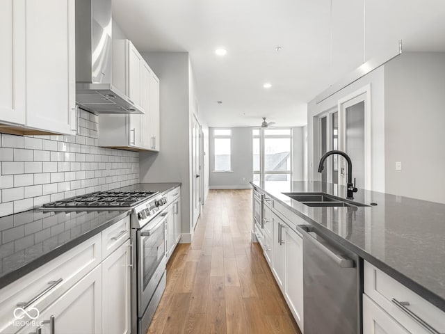 kitchen with backsplash, light wood-style flooring, appliances with stainless steel finishes, a sink, and wall chimney range hood