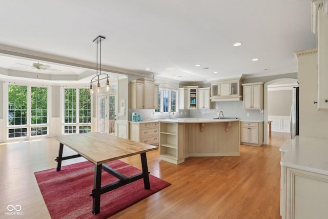 kitchen with arched walkways, a ceiling fan, ornamental molding, cream cabinetry, and light countertops