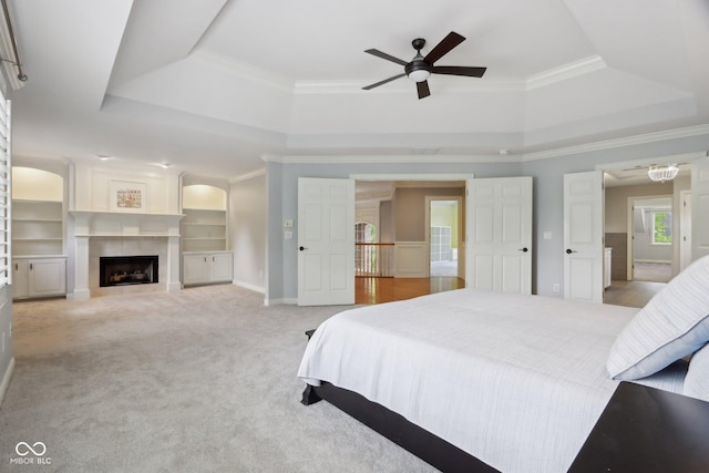 carpeted bedroom with a tray ceiling, ornamental molding, a fireplace, and baseboards