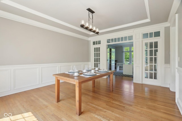 dining space with a decorative wall, crown molding, light wood finished floors, french doors, and a wainscoted wall