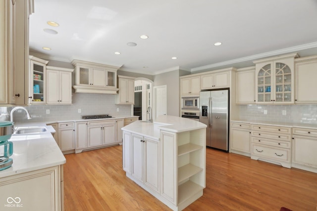 kitchen with stainless steel appliances, a sink, cream cabinetry, arched walkways, and crown molding