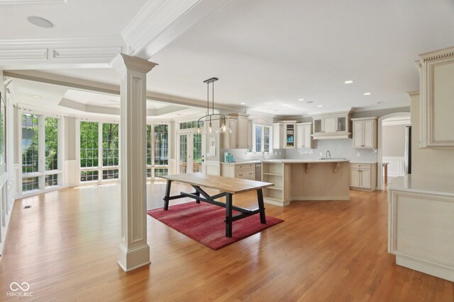 kitchen with ornate columns, cream cabinetry, a sink, tasteful backsplash, and glass insert cabinets