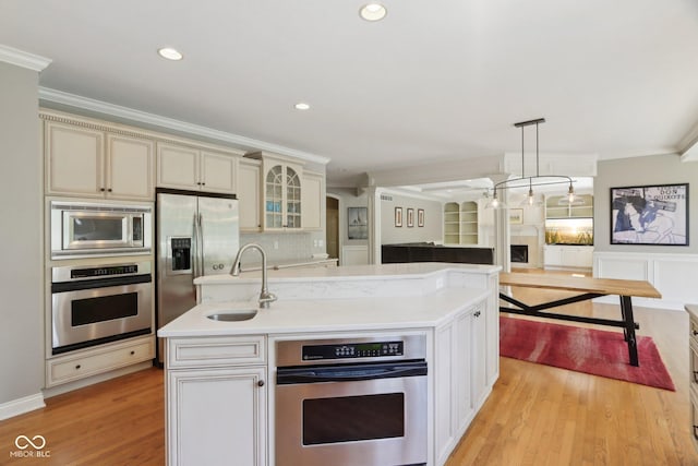 kitchen with stainless steel appliances, a sink, crown molding, light wood-style floors, and light countertops