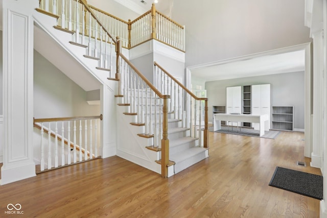 staircase featuring a towering ceiling, wood finished floors, and baseboards