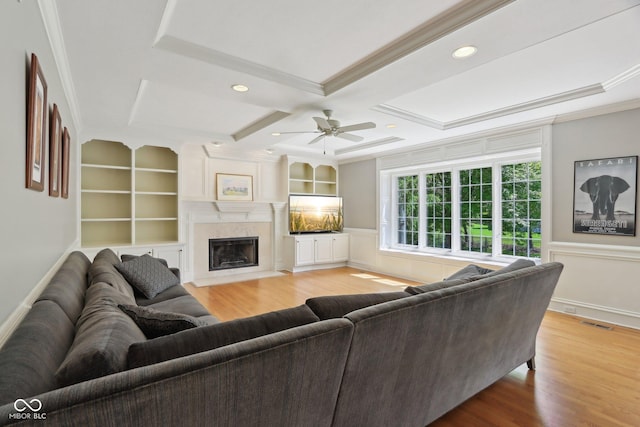 living area featuring ornamental molding, ceiling fan, light wood-style flooring, a fireplace, and coffered ceiling