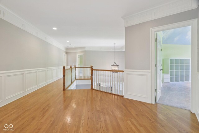hall featuring ornamental molding, a decorative wall, light wood finished floors, a wainscoted wall, and a chandelier