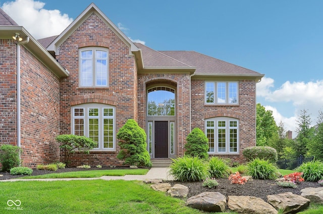 view of front of house with brick siding, roof with shingles, and a front lawn
