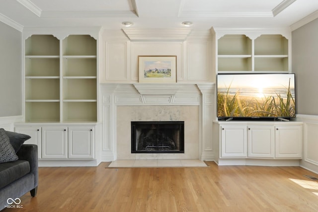 unfurnished living room featuring ornamental molding, light wood finished floors, built in features, and a premium fireplace