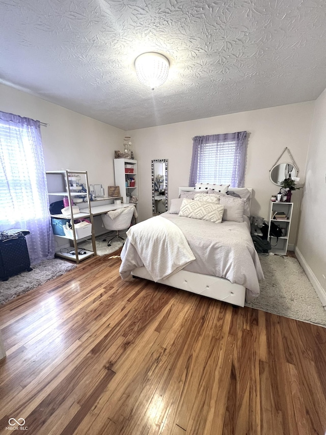 bedroom with a textured ceiling, baseboards, and wood finished floors