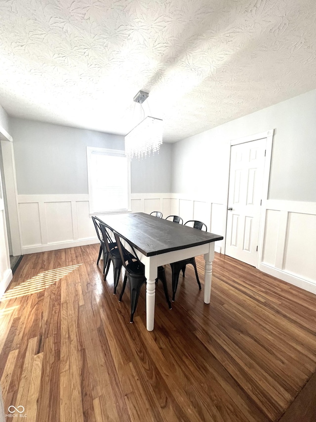 dining area featuring a textured ceiling, wainscoting, wood finished floors, and an inviting chandelier