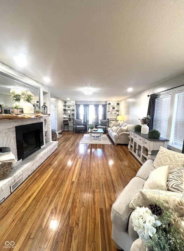 living area featuring a brick fireplace, a textured ceiling, and wood finished floors