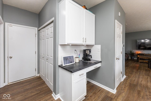 kitchen featuring baseboards, decorative backsplash, dark countertops, dark wood-style flooring, and white cabinetry