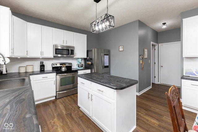 kitchen featuring dark wood-style flooring, dark countertops, backsplash, appliances with stainless steel finishes, and a sink