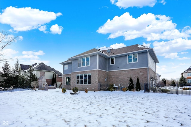 snow covered rear of property with fence and brick siding