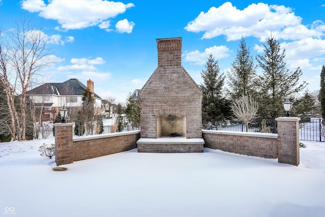 snow covered patio with fence and an outdoor brick fireplace