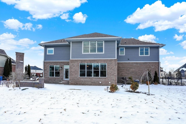 snow covered rear of property featuring brick siding and fence