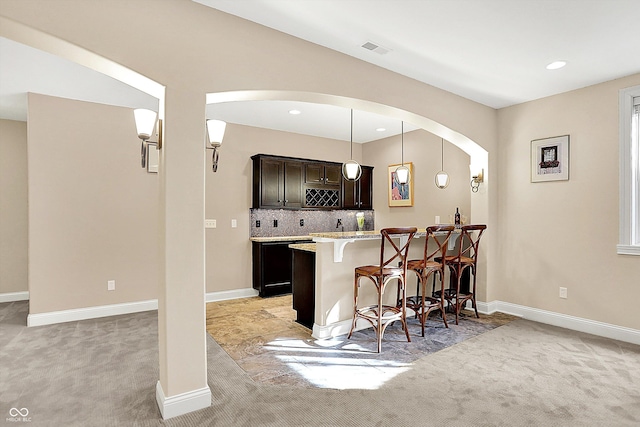 kitchen featuring tasteful backsplash, visible vents, baseboards, light colored carpet, and a kitchen bar