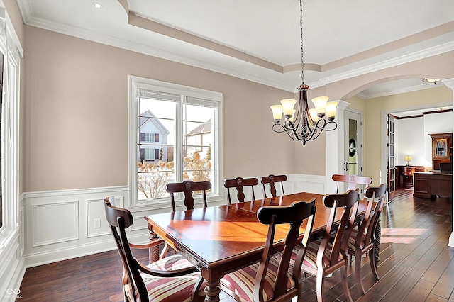 dining room featuring dark wood-style floors, a wainscoted wall, arched walkways, and a raised ceiling