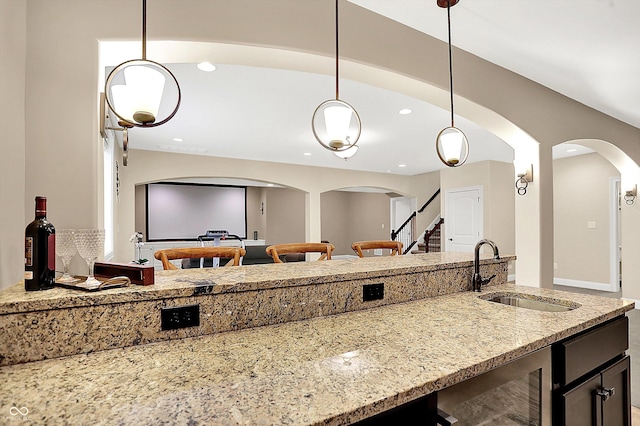 kitchen with light stone countertops, wine cooler, open floor plan, hanging light fixtures, and a sink