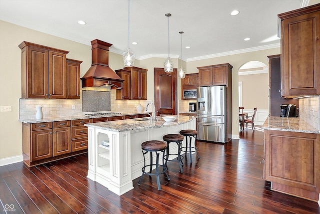 kitchen with a breakfast bar, custom exhaust hood, arched walkways, dark wood-style flooring, and appliances with stainless steel finishes