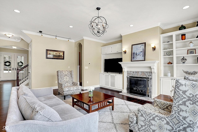 living room with arched walkways, dark wood finished floors, a high end fireplace, and ornamental molding