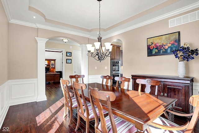 dining space with a wainscoted wall, visible vents, ornate columns, dark wood-style flooring, and arched walkways