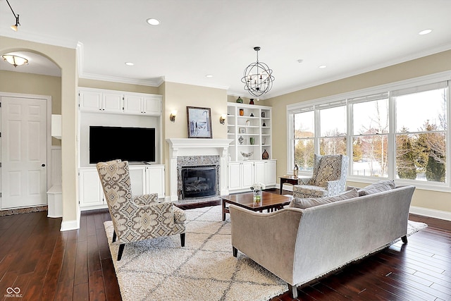 living area featuring a high end fireplace, ornamental molding, arched walkways, and dark wood-style flooring