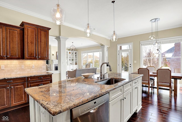 kitchen featuring a kitchen island with sink, a sink, decorative columns, dishwasher, and dark wood-style flooring