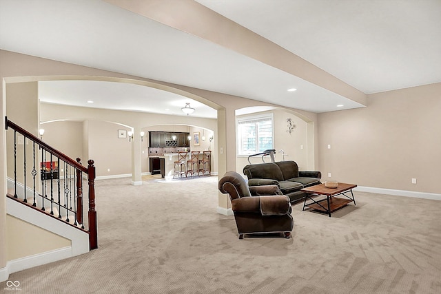 living room featuring stairway, arched walkways, light colored carpet, and baseboards