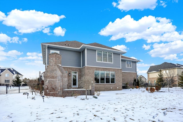 snow covered back of property with brick siding and fence