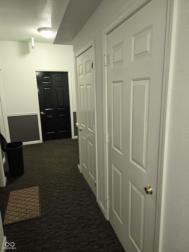 hall featuring a textured ceiling, dark carpet, and baseboards