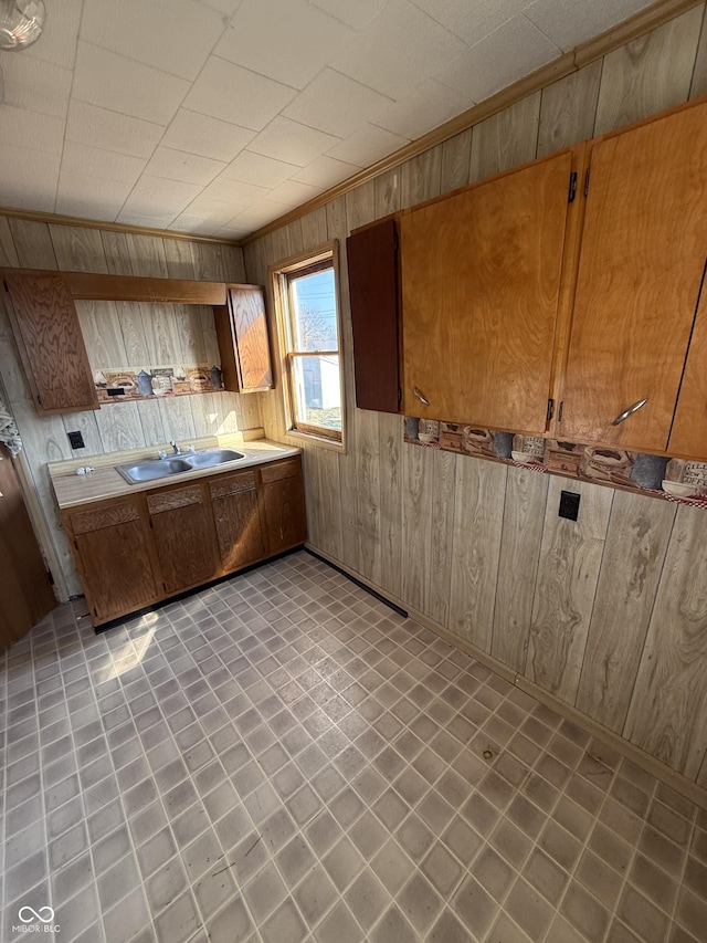 kitchen with light countertops, wooden walls, brown cabinets, and a sink