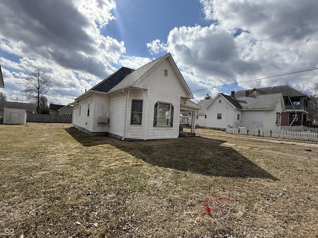 rear view of house featuring a lawn and fence