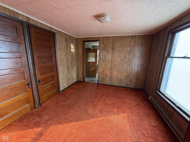 carpeted spare room featuring wooden walls, a wealth of natural light, and a baseboard radiator