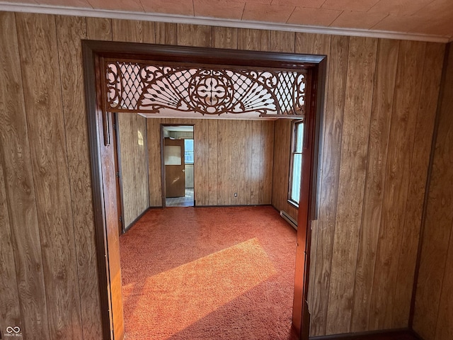 spare room featuring a baseboard radiator, carpet, wood walls, and ornamental molding